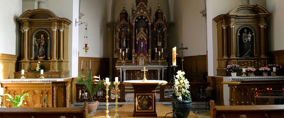 An ornate church interior with a central altar, pews, and religious statues.