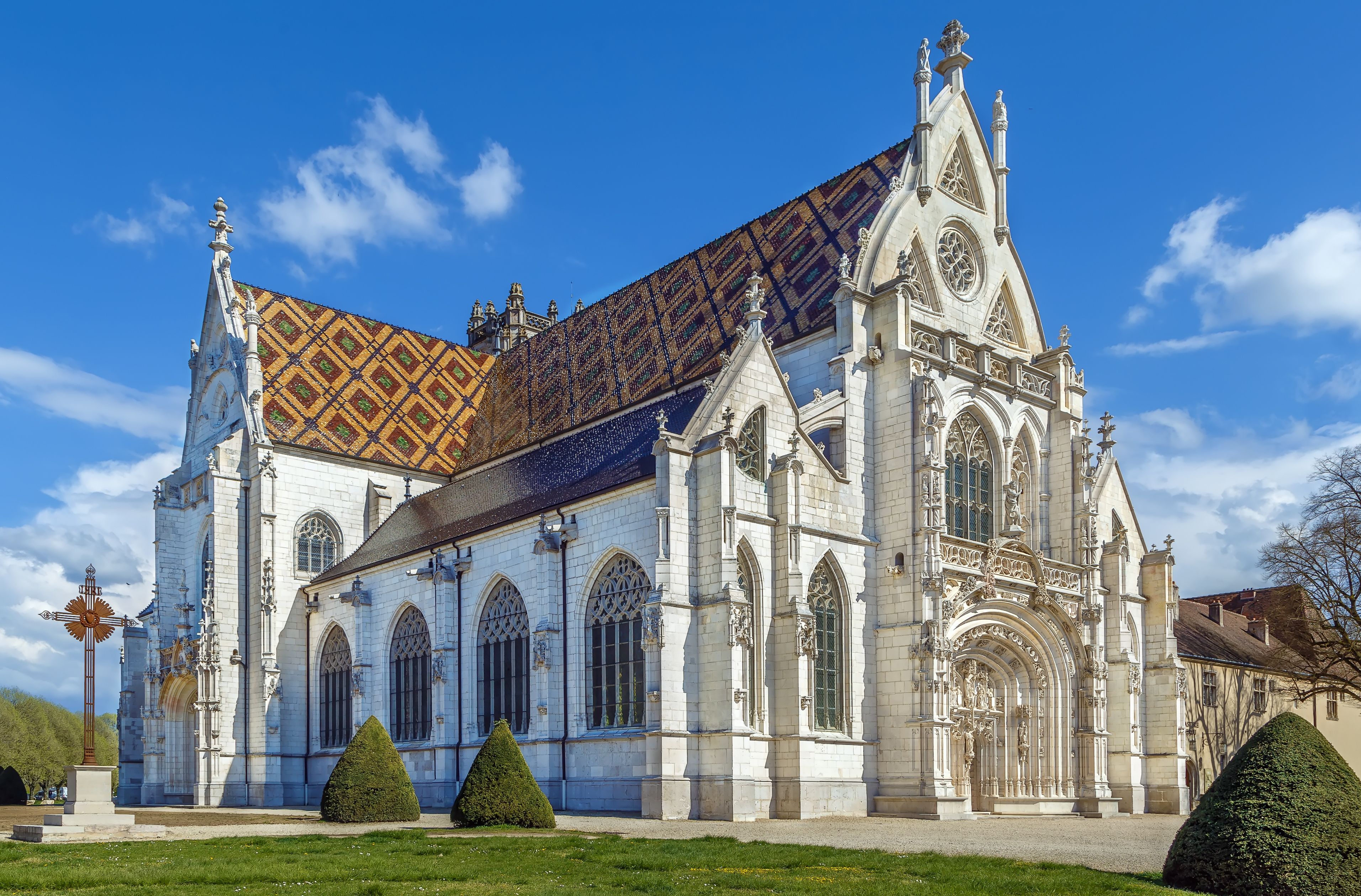 En historisk katedral med utsmyckad gotisk arkitektur, ett färgglatt tak täckt med kakel och välskötta trädgårdar.