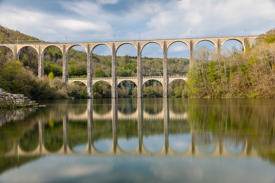 Eine steinerne Viaduktbogenbrücke überspannt einen Fluss, umgeben von Bäumen und Hügeln.
