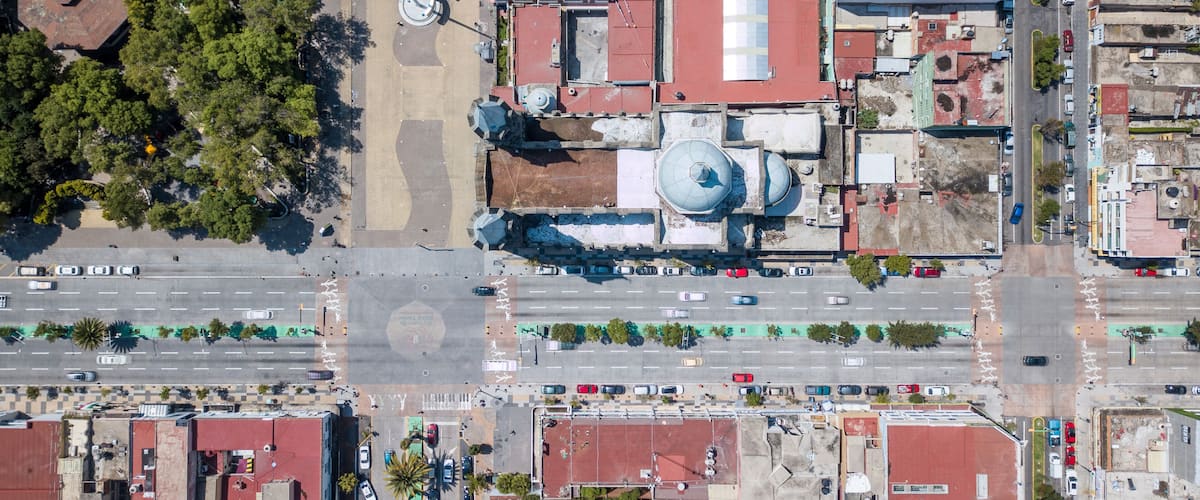 An aerial view of a city with a prominent mosque, intersecting roads, and surrounding greenery.