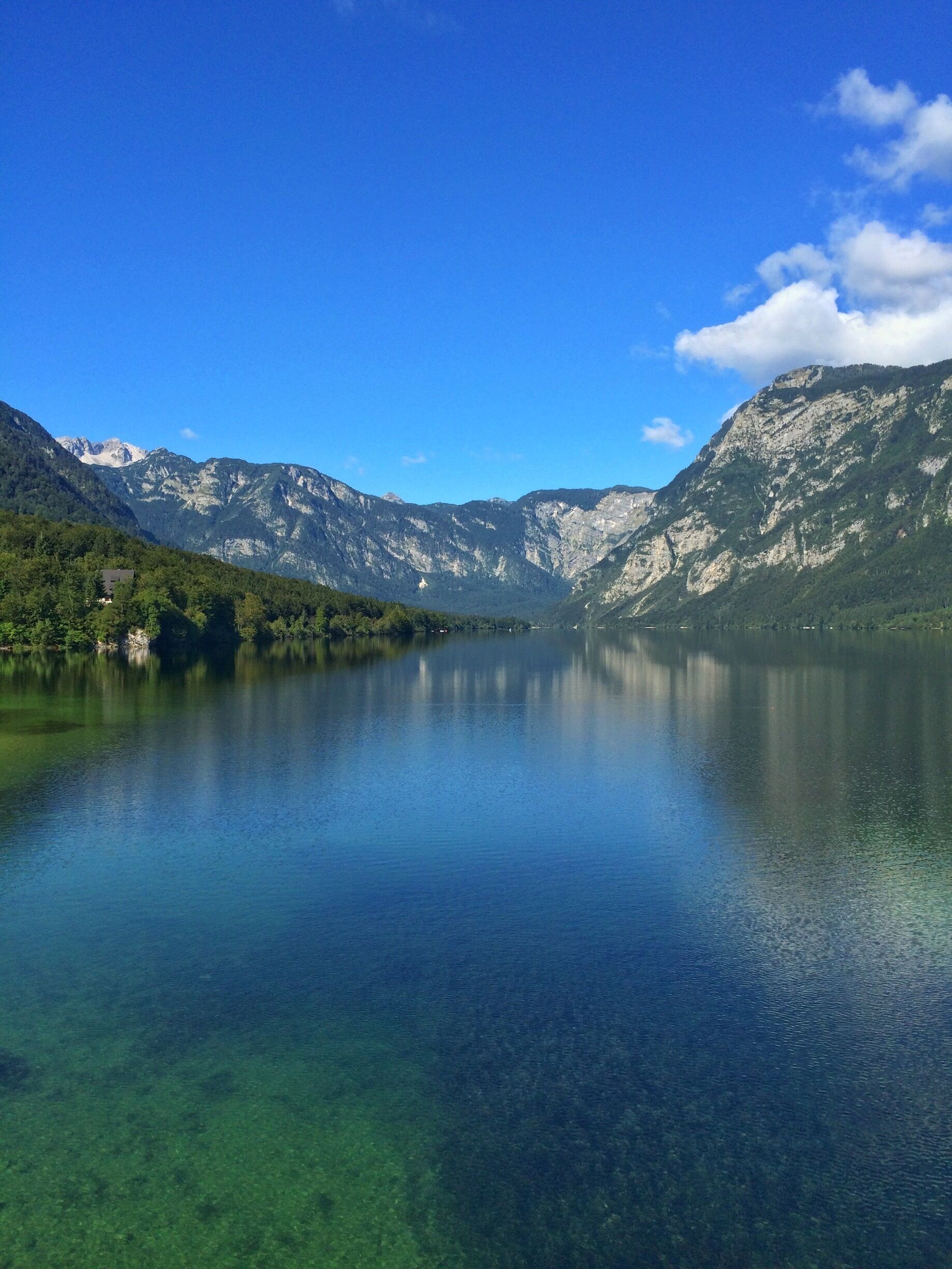 A clear lake surrounded by mountains with a small house on the left.