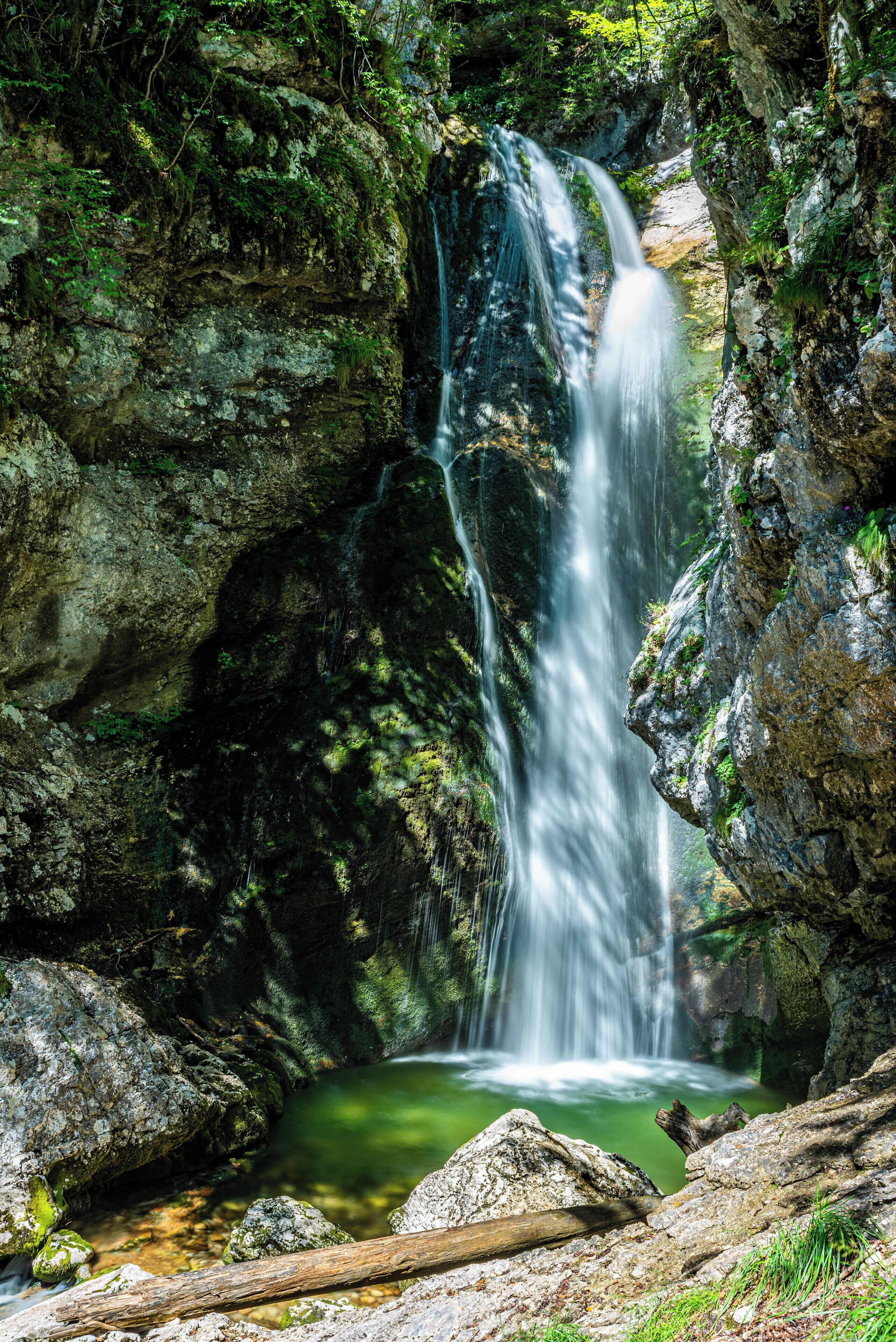 A waterfall cascading down a rocky cliff into a pool surrounded by lush greenery.