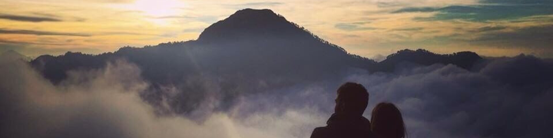 Una pareja de pie en la cima de una montaña, con el amanecer de fondo.