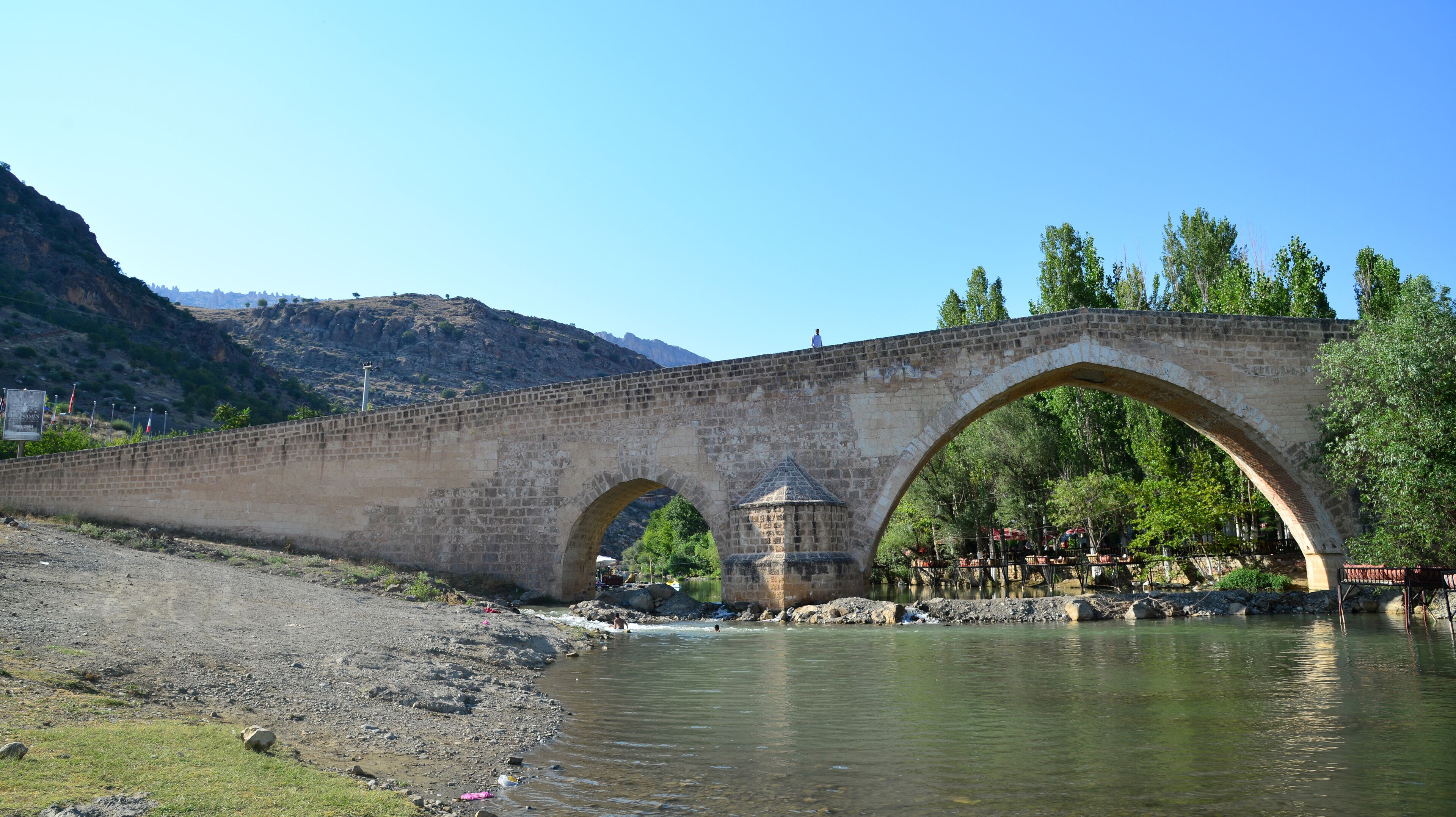 A stone bridge over a river with a small tower and a person standing on top.