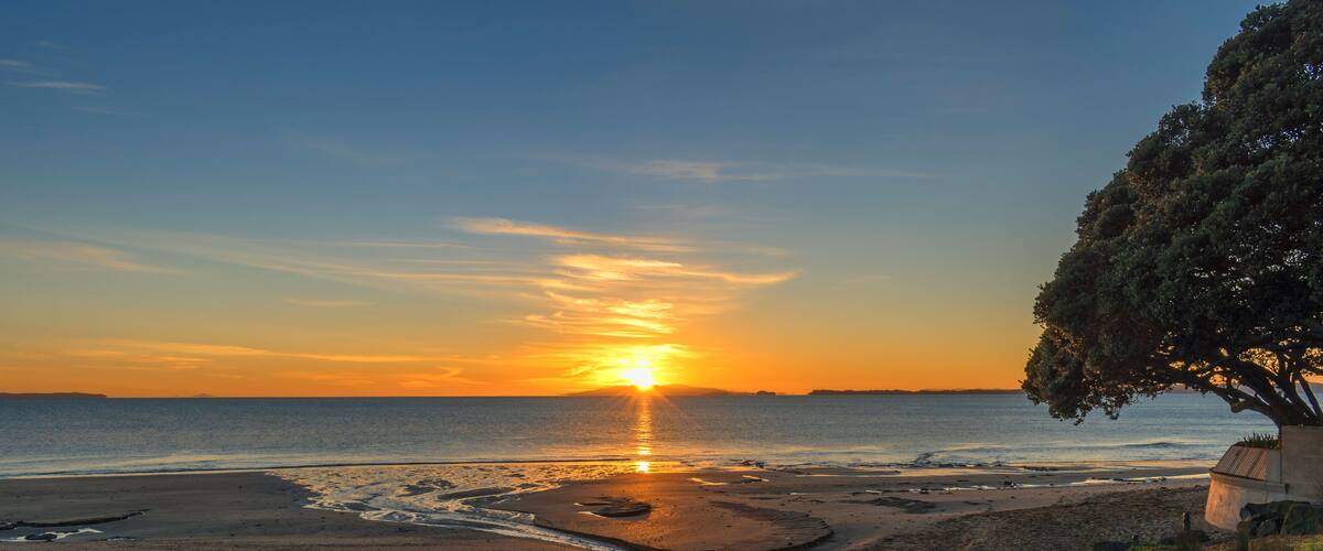 Een zonsondergang boven een strand met een rivier die erdoorheen stroomt.
