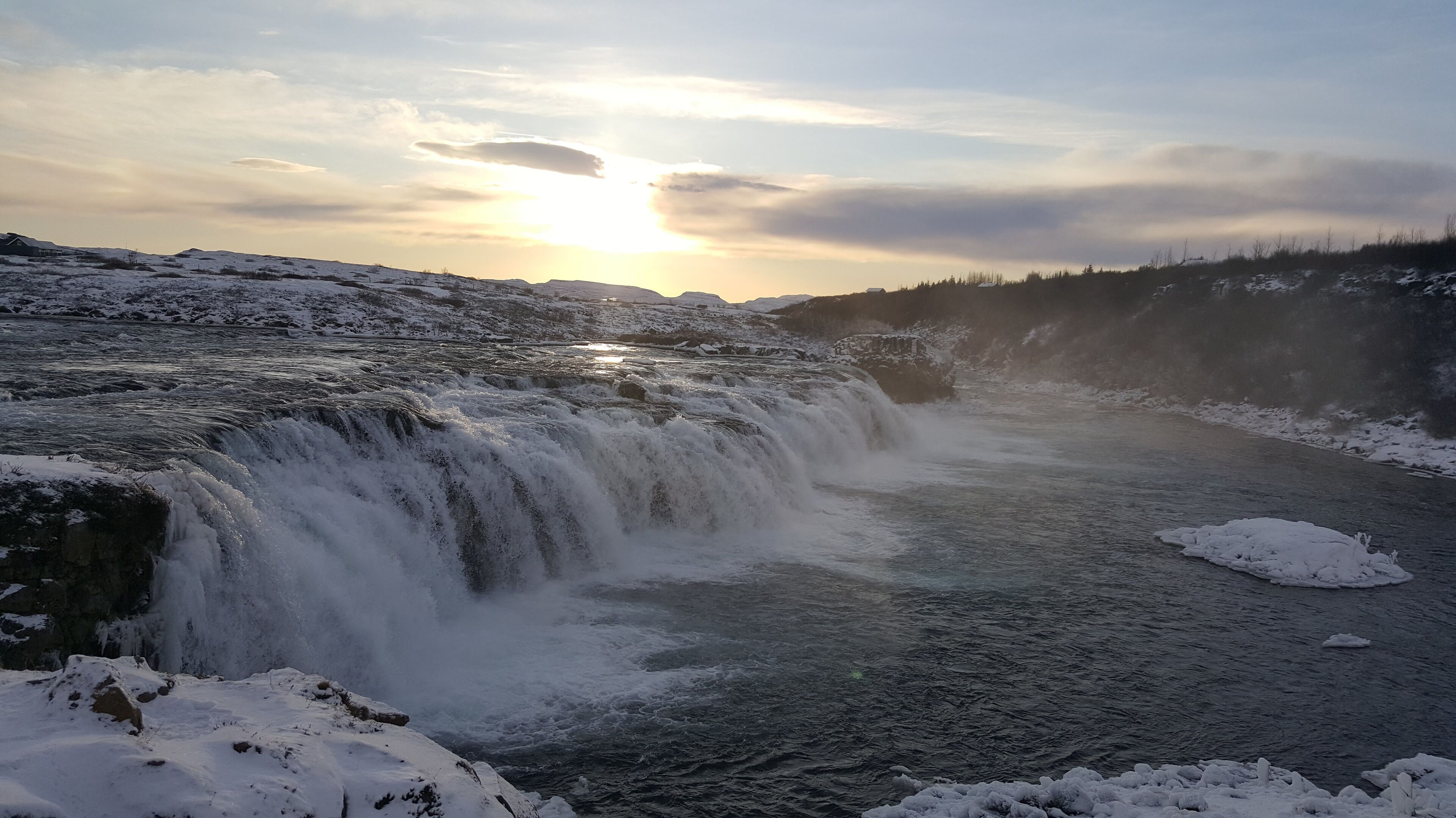 A waterfall cascading over snow-covered rocks with a sunset in the background.