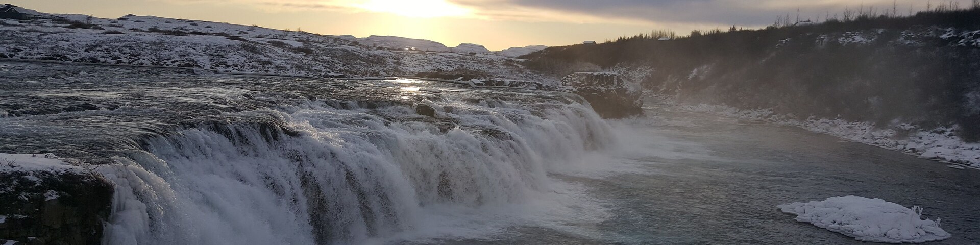 A waterfall cascading over snow-covered rocks with a sunset in the background.