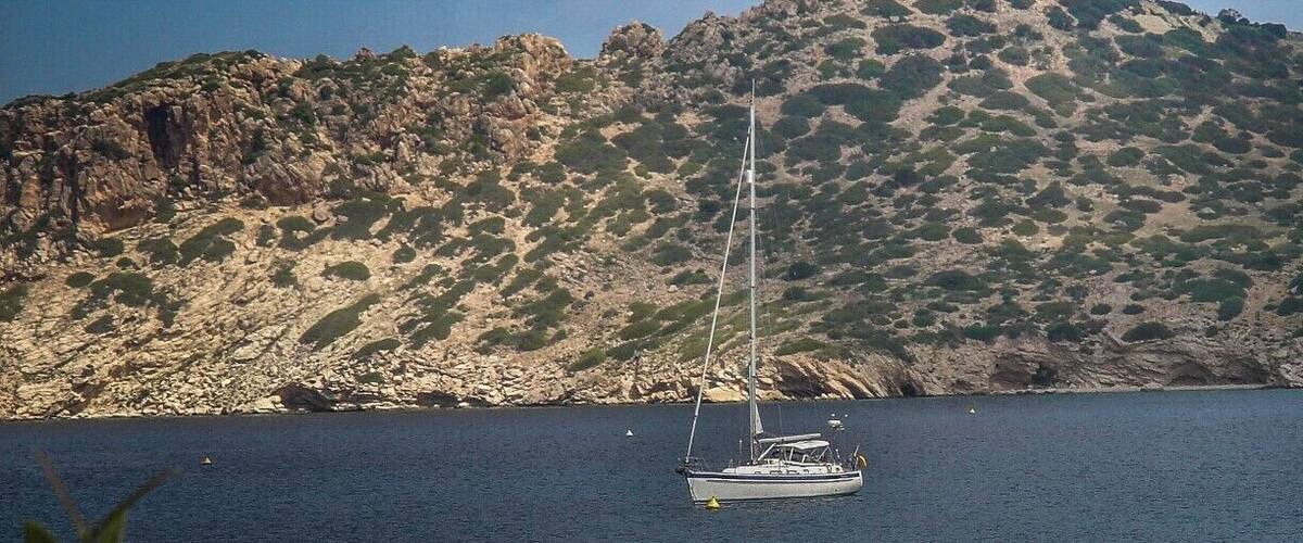 A sailboat on calm waters with a rocky hill and a castle in the background.