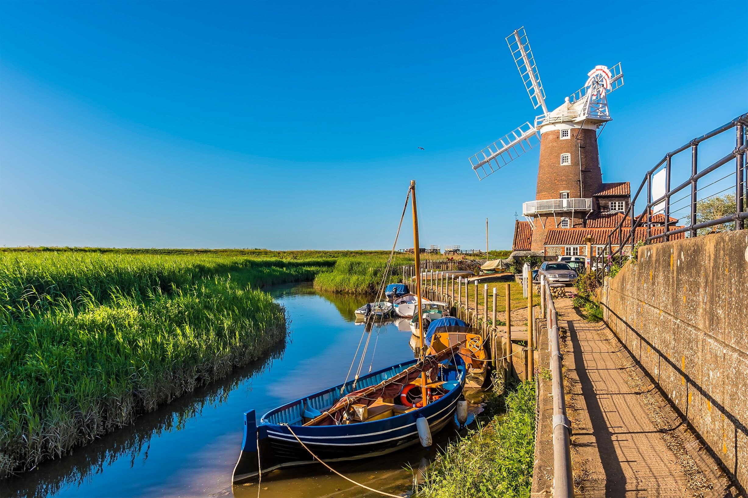 A windmill, a canal, boats, and a grassy field.
