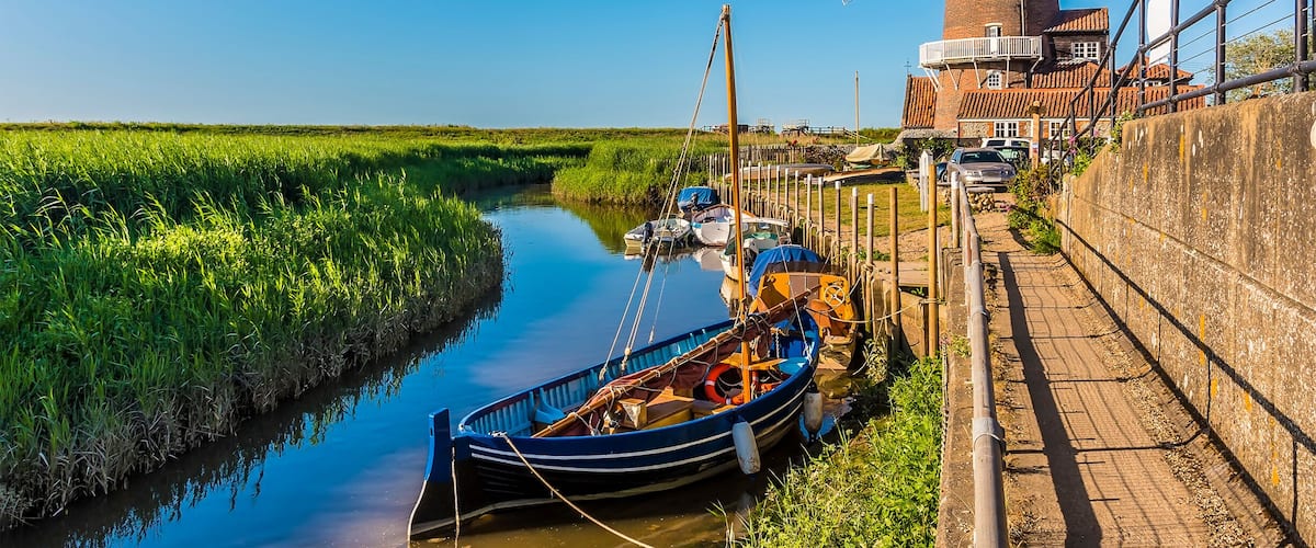 A windmill, a canal, boats, and a grassy field.
