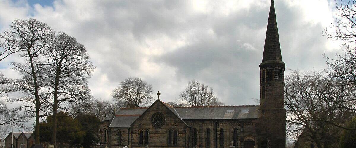 A church with a tall spire and a graveyard with numerous headstones.