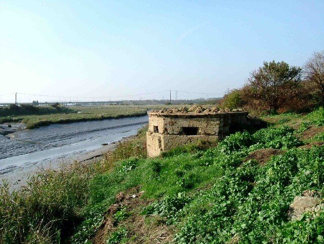 Pillbox on Benfleet Creek. This pillbox on Benfleet Creek has seen better days its concrete skin has fallen away revealing that this block house is of brick construction which would not afford much protection against a tank round. In the background you can just see the A130 to Canvey Island