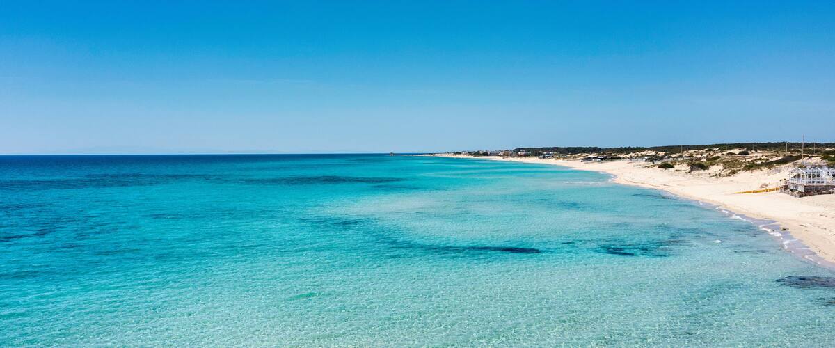 A beach with clear turquoise waters and a sandy shore.