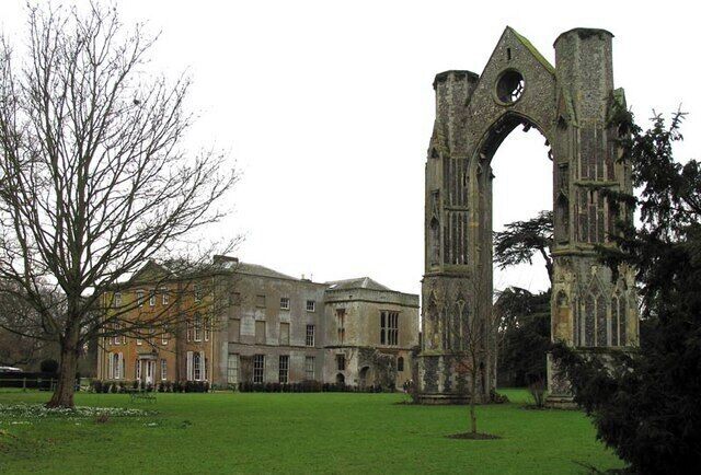 A historic stone archway with a large circular window, surrounded by a well-maintained lawn and a building in the background.