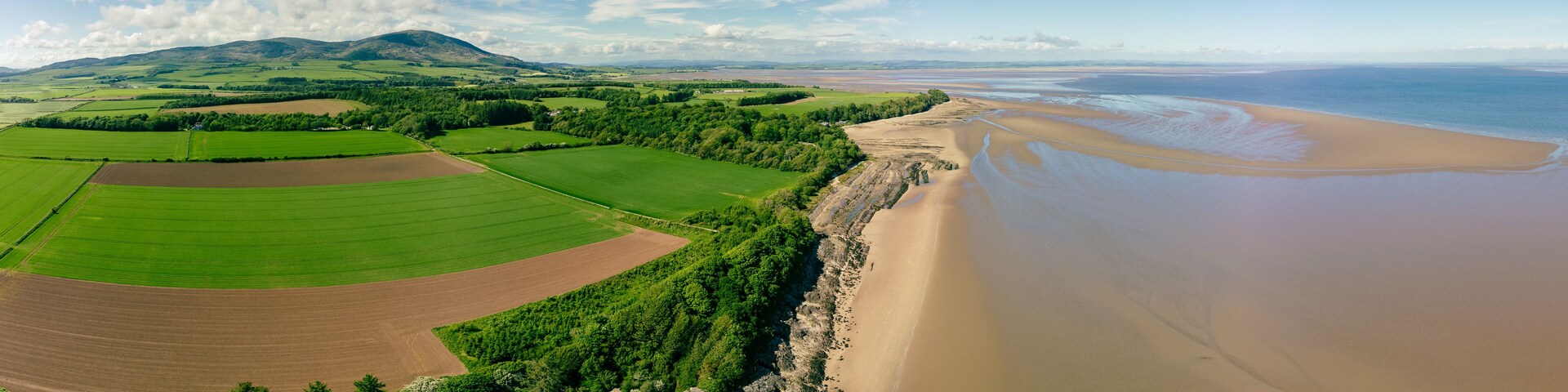 Un paisaje costero con una playa arenosa, campos verdes y un río.