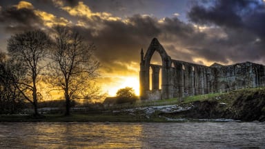 Une cathédrale en ruine, avec une rivière au premier plan et un coucher de soleil en arrière-plan.