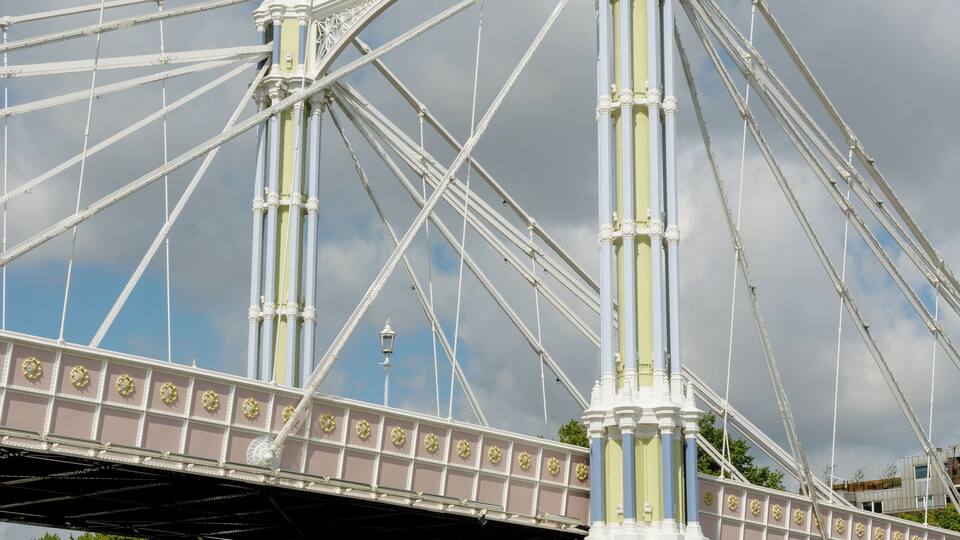 A large suspension bridge with intricate white and yellow details, spanning over a river with boats.