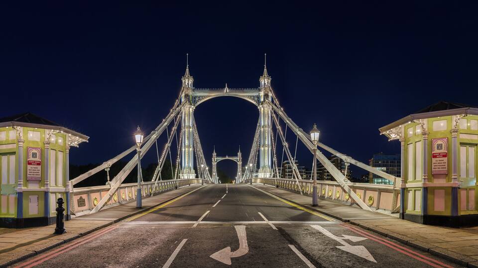 A brightly lit bridge at night with two guardhouses on either side.
