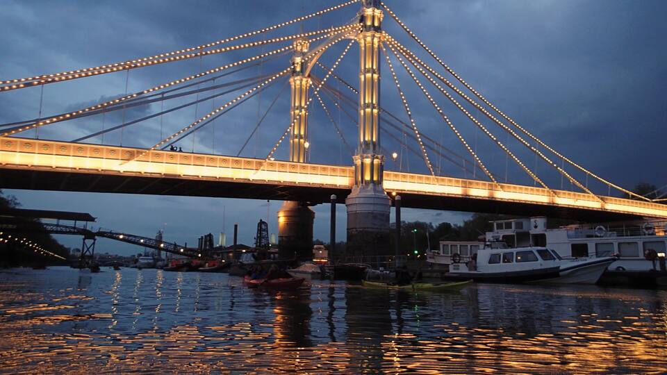 A bridge with illuminated cables and a central tower, reflecting on the water.