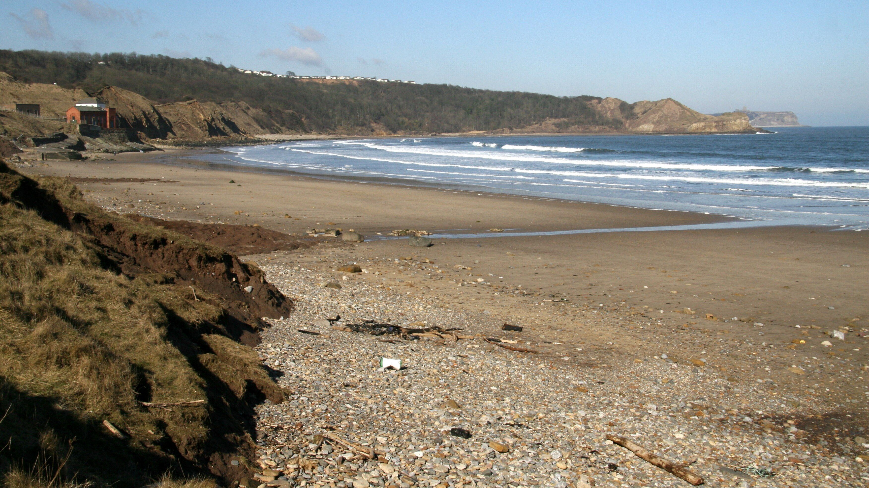 Cayton Bay and beach The photograph is taken from near to the bottom of a steep, metalled path ( https://www.geograph.org.uk/photo/1776491 ) from the cliff top and car park ( https://www.geograph.org.uk/photo/1776414 ) above. In the left foreground can be seen the boulder clay that the local cliff is made from and the cause of so much land slippage in recent years. For more, follow this link to the BBC news web site: http://news.bbc.co.uk/1/hi/england/north_yorkshire/8550186.stm . The red bricked building (upper left) is the Yorkshire Water Cayton land drainage pumping station. For another photograph taken some 150metres nearer the pumping station, click here: https://www.geograph.org.uk/photo/1777802 . The bungalows on the cliff top in the distance are built on the site of the former NALGO holiday camp and have been the subject of press interest in recent years because of the previously mentioned land slippage. For more, follow this link to the BBC news web site: http://news.bbc.co.uk/1/hi/uk/8578583.stm . At the end of the bay is Knipe Point (TA 06513 85470), which is sometimes referred to as Osgodby Nab. (The OS map erroneously refers to Osgodby Point) and, beyond that, in the distance can be seen the castle headland at Scarborough (TA 05051 89213).