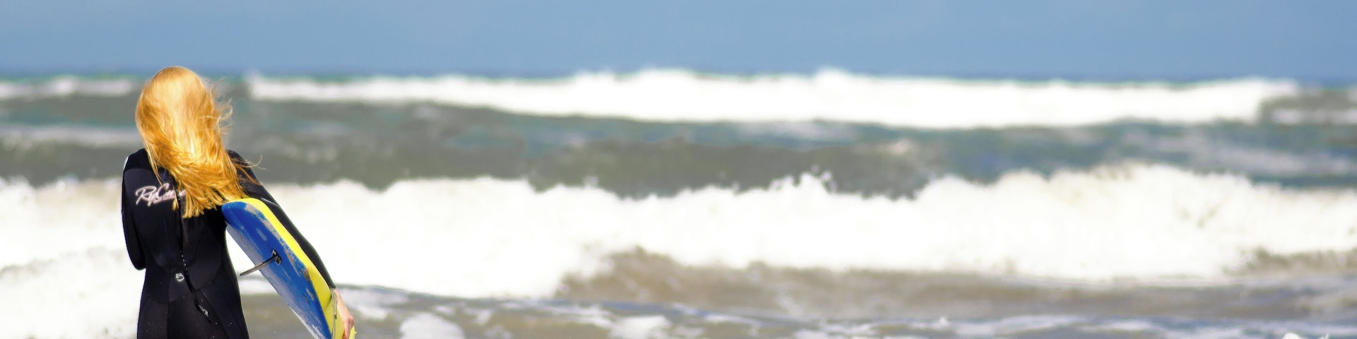 Uma pessoa com fato de mergulho carregando uma prancha de surf na praia.