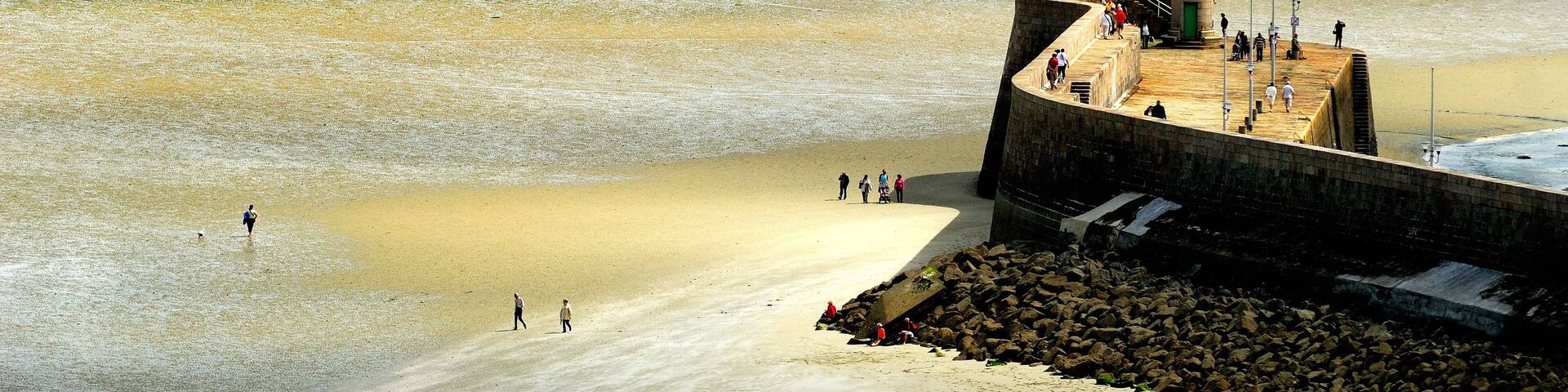A lighthouse on a sandy beach with people walking around it.