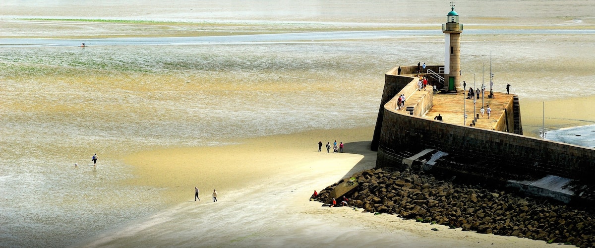 A lighthouse on a sandy beach with people walking around it.