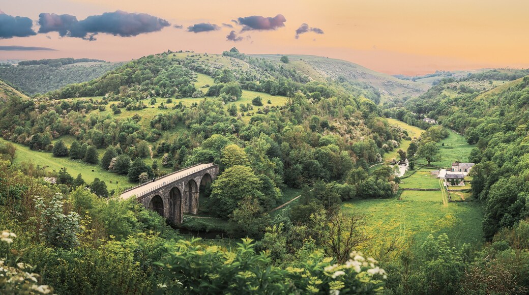 Une vallée avec un pont de pierre, une végétation luxuriante et une maison située sur une colline.