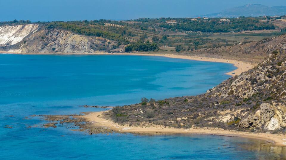 A coastal landscape with a sandy beach, rocky cliffs, and a clear blue sea.