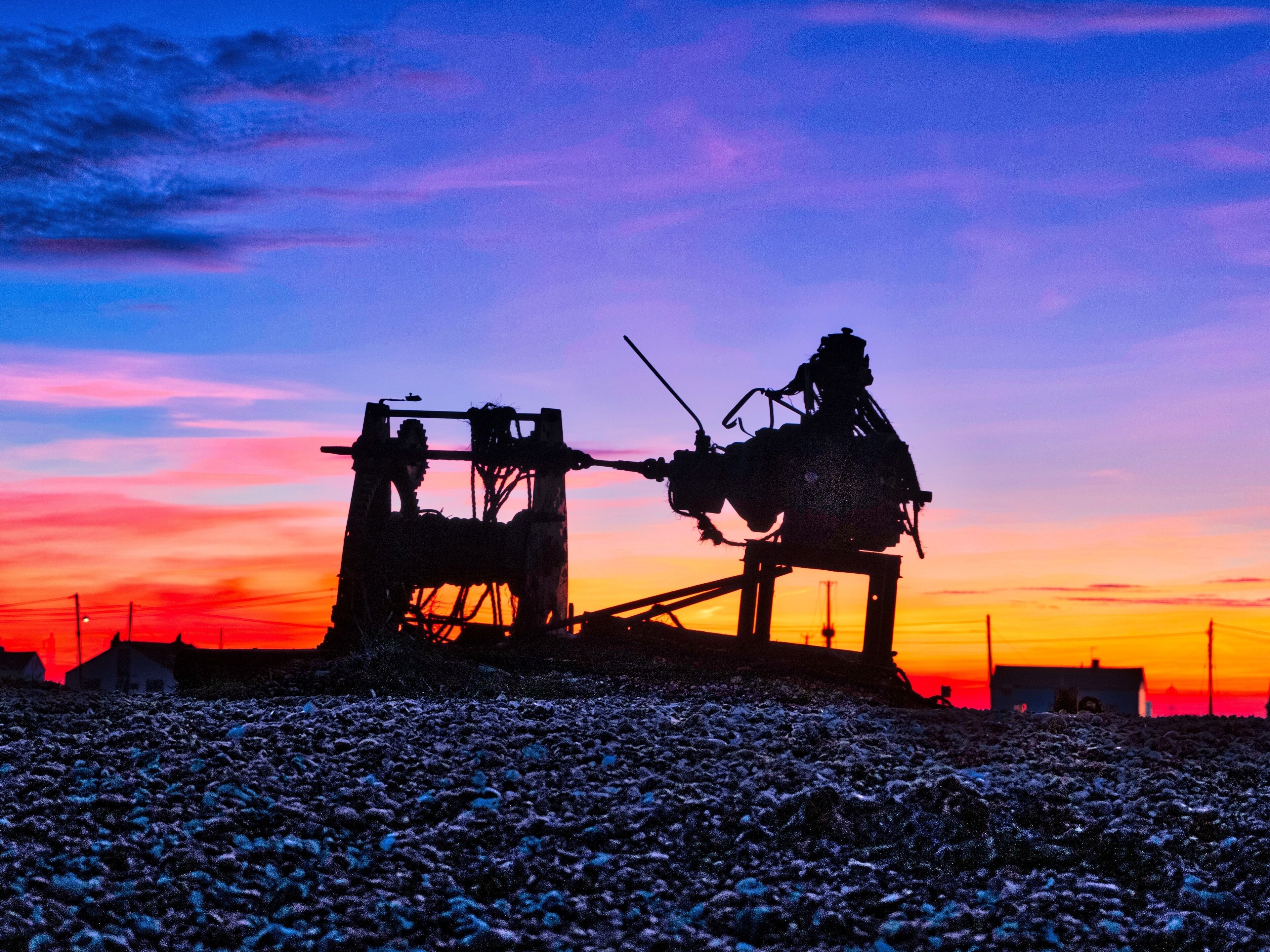 Sunset over Dungeness beach with the silhouette of a fishing boat winch in the foreground.
