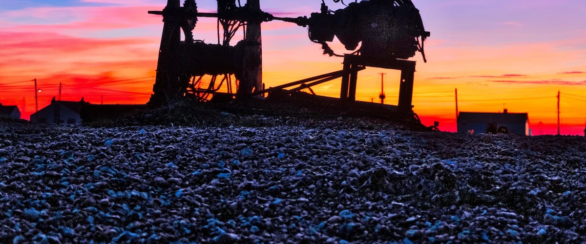 Sunset over Dungeness beach with the silhouette of a fishing boat winch in the foreground.