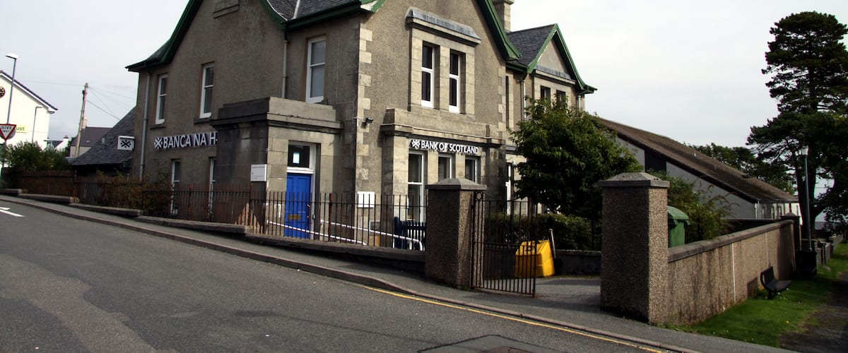 A two-story building with a green roof and a sign that reads "Bank of Scotland."