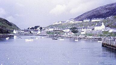 A coastal town with houses along the shore, a pier extending into the water, and several boats.
