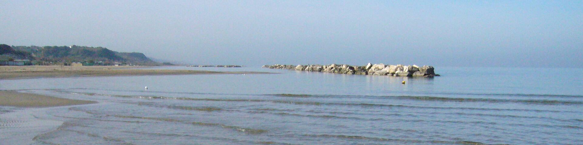 A calm beach with gentle waves, a rocky outcrop in the distance, and a clear sky.