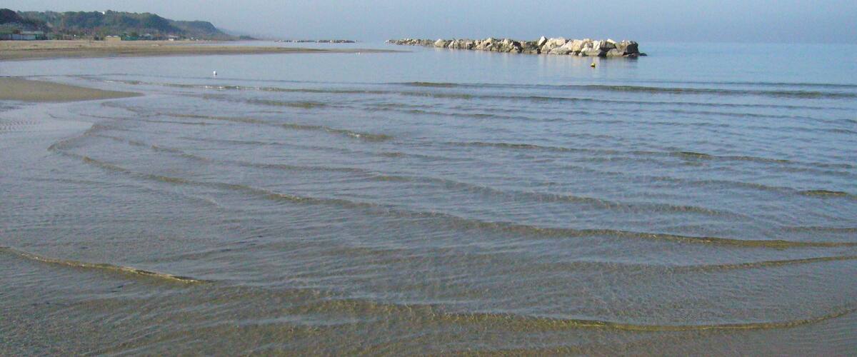 A calm beach with gentle waves, a rocky outcrop in the distance, and a clear sky.