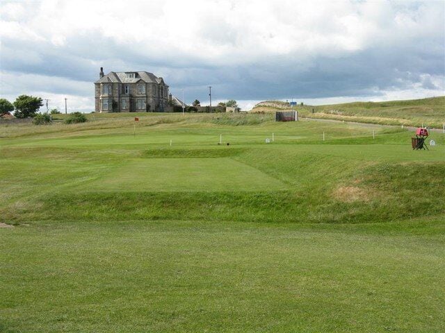 A golf course with a clubhouse, a flag, and a distant hill.