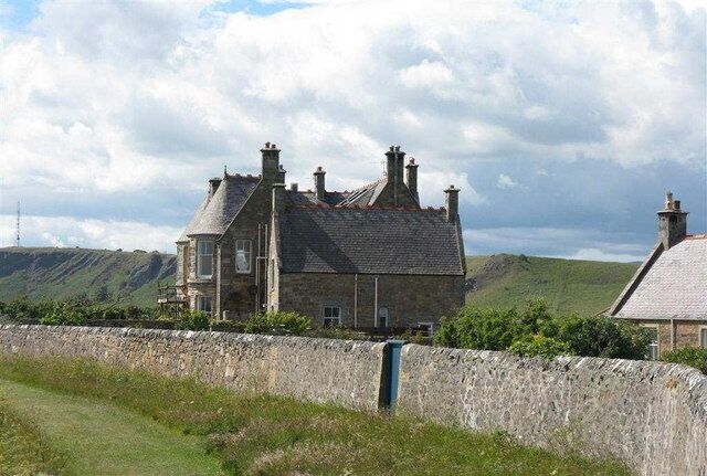 A stone house with a steep roof, surrounded by a stone wall and lush green hills.