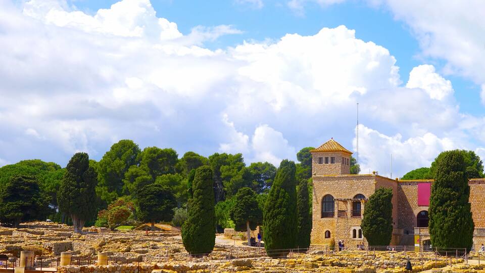 An ancient stone structure with a tower, surrounded by trees and ruins.
