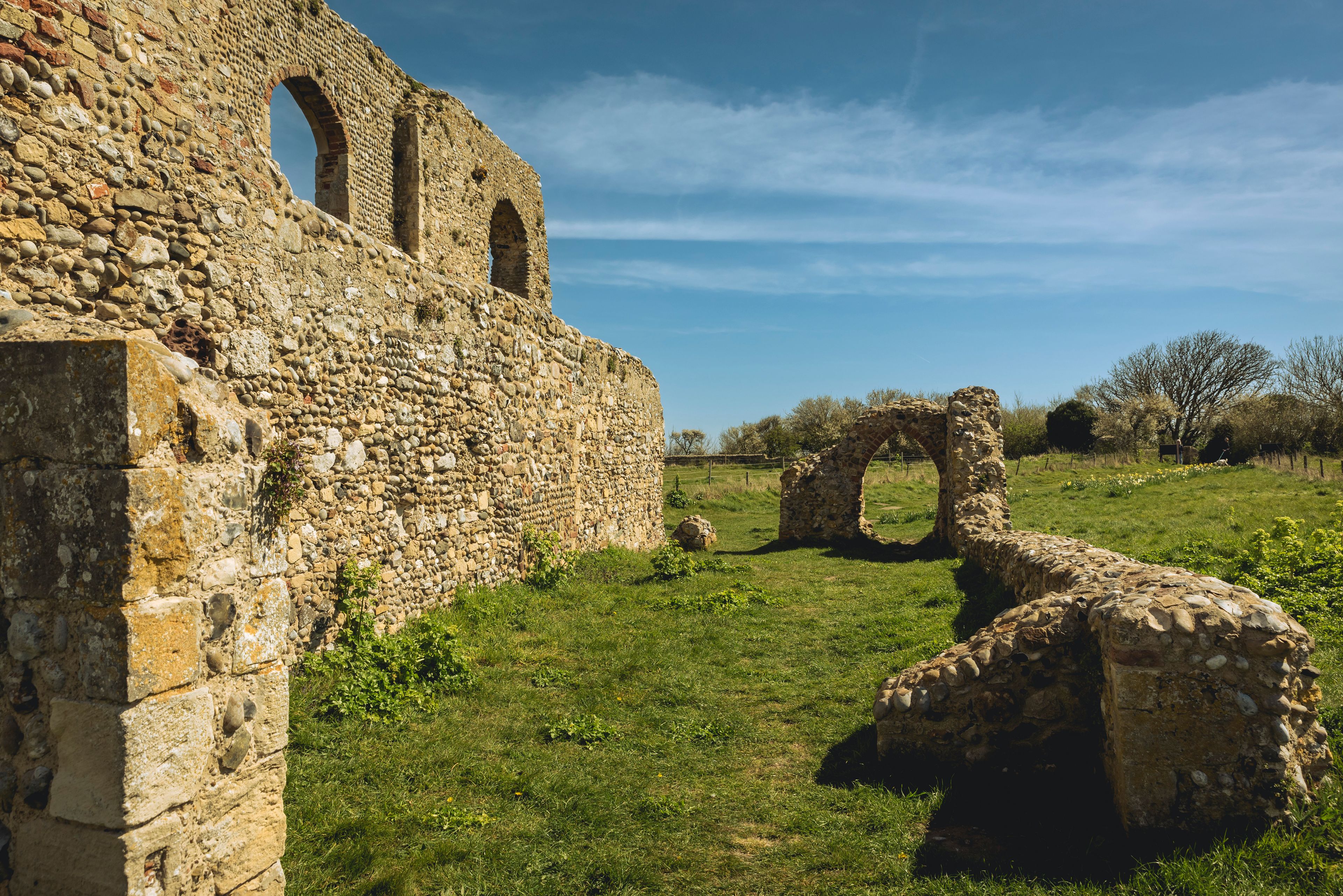 Antiguas ruinas de piedra con arcos y muros, rodeadas por un campo cubierto de hierba y árboles.
