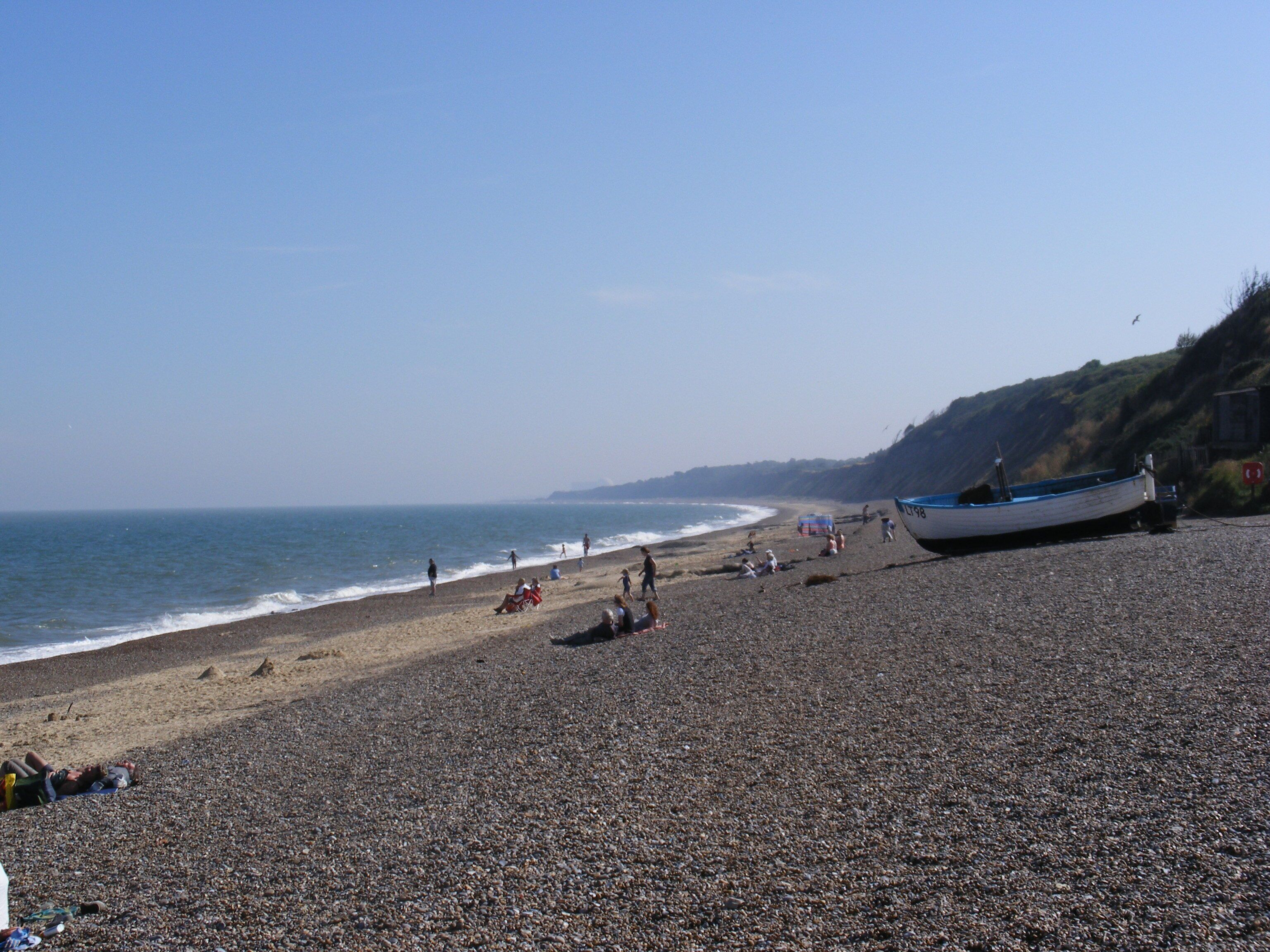 A pebbled beach with a boat on the right and people relaxing.