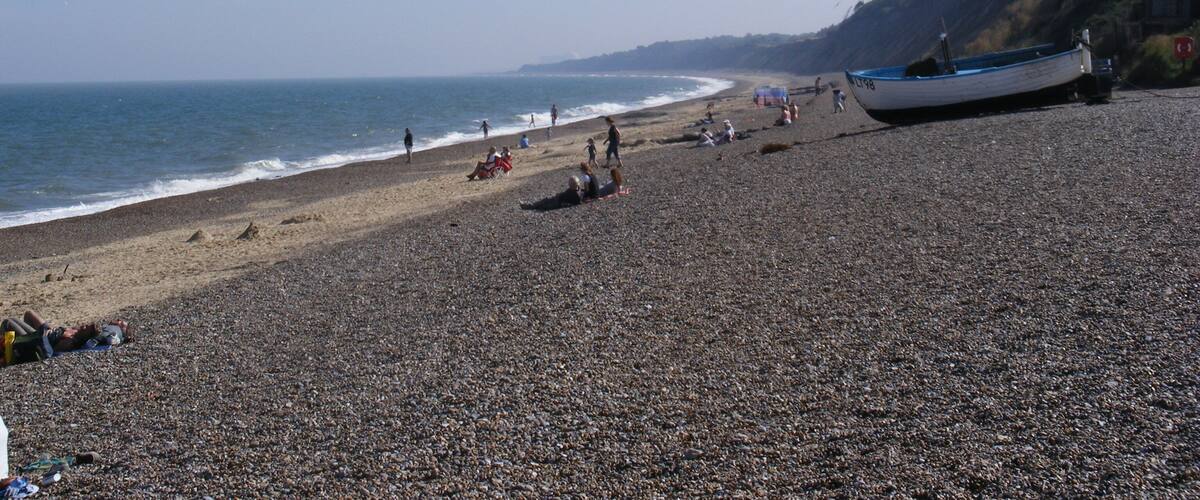 A pebbled beach with a boat on the right and people relaxing.