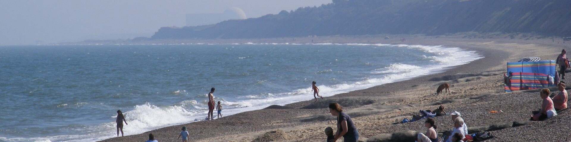 Una playa de canto rodado con gente tomando el sol y paseando por la orilla.