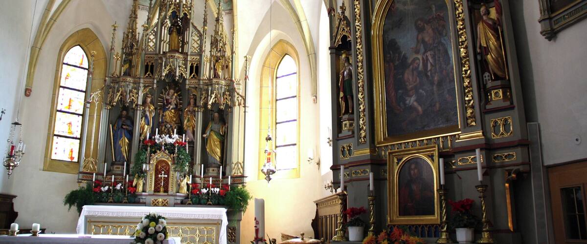 An ornate church interior with a high vaulted ceiling, a large altar, and religious paintings.
