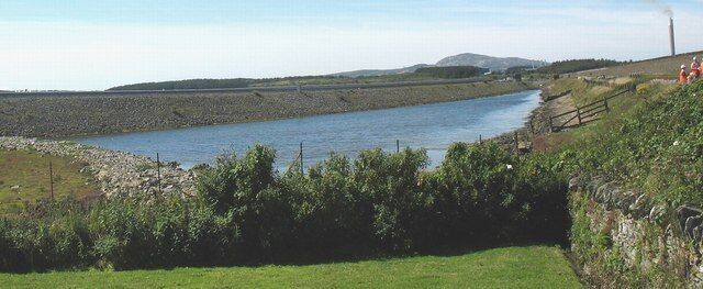 A river flowing through a rural landscape with grassy banks and a stone wall.