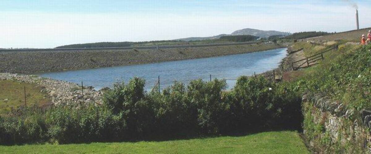 A river flowing through a rural landscape with grassy banks and a stone wall.
