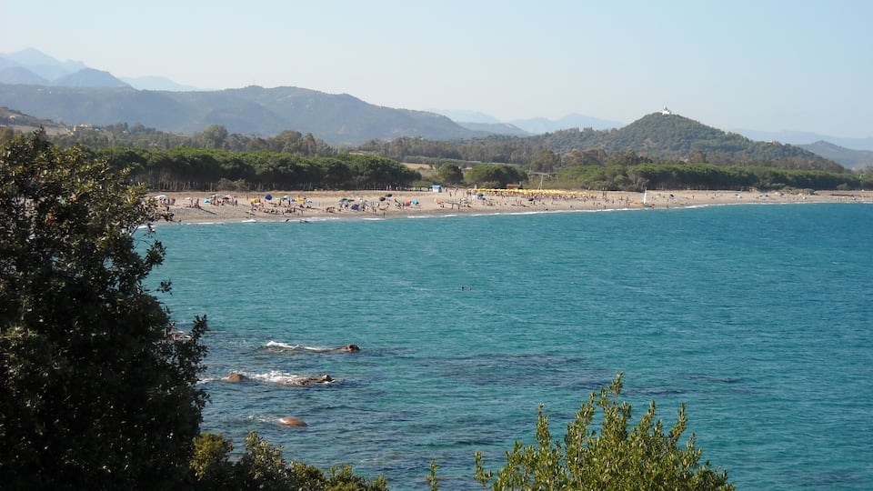 A coastal beach with clear blue waters, a sandy shore, and distant mountains.