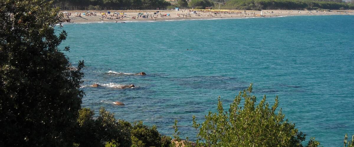 A coastal beach with clear blue waters, a sandy shore, and distant mountains.