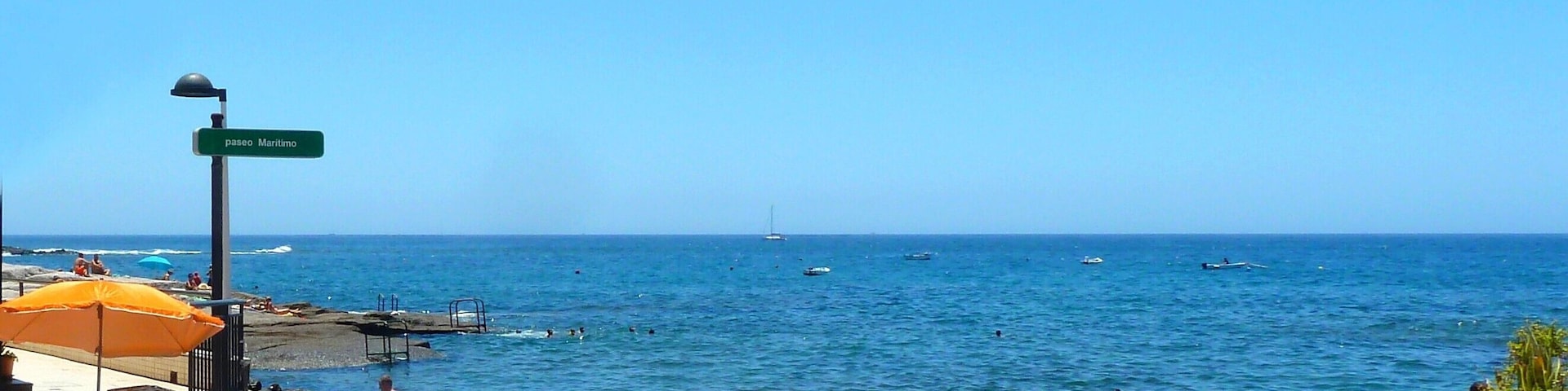 Una playa con barcos, gente y un cielo azul despejado.