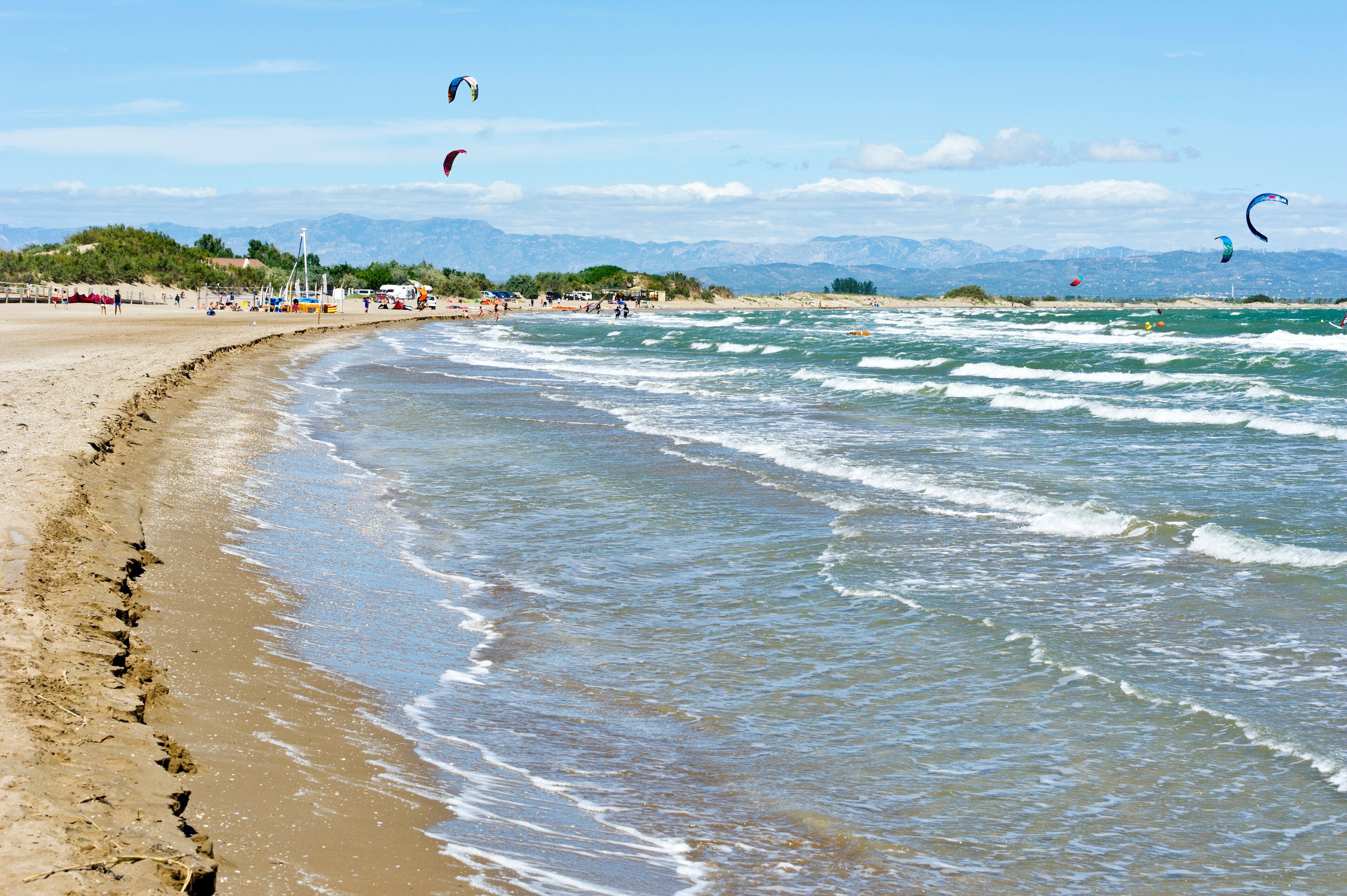 A sandy beach with waves, a clear sky, and mountains in the background.
