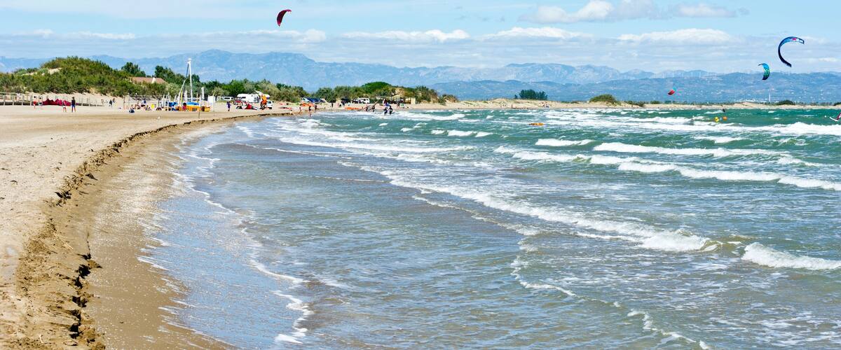 A sandy beach with waves, a clear sky, and mountains in the background.